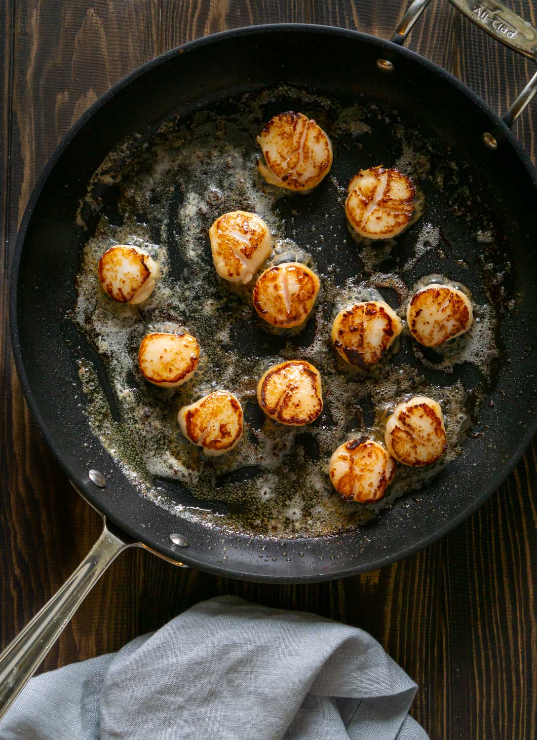 Seared scallops in a pan with butter and a grey napkin to the side.