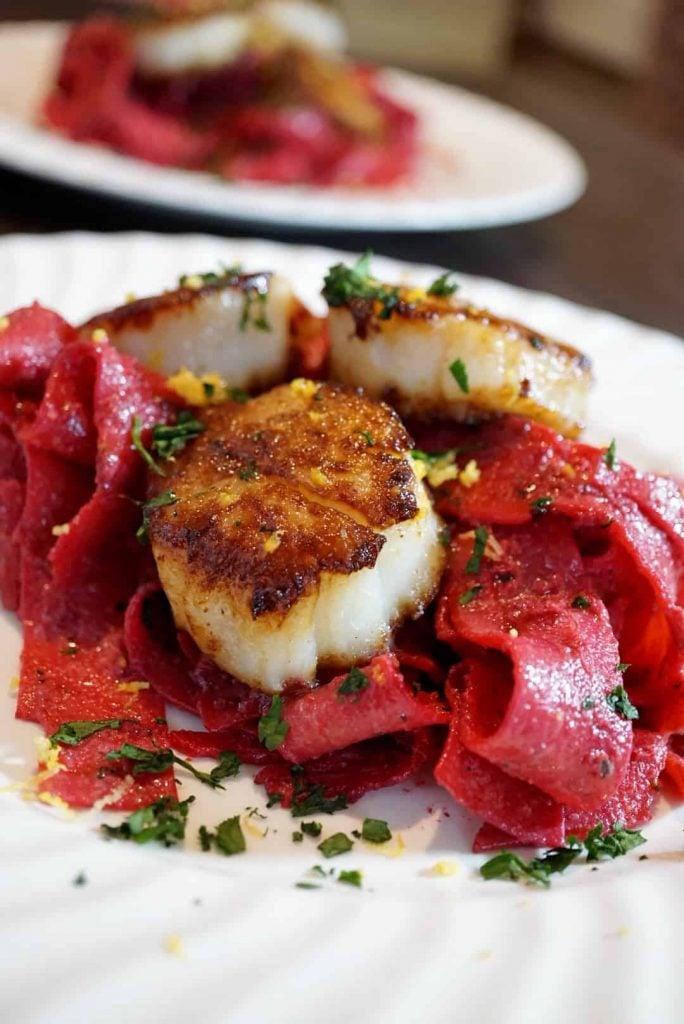 beet pappardelle with scallops on a white plate