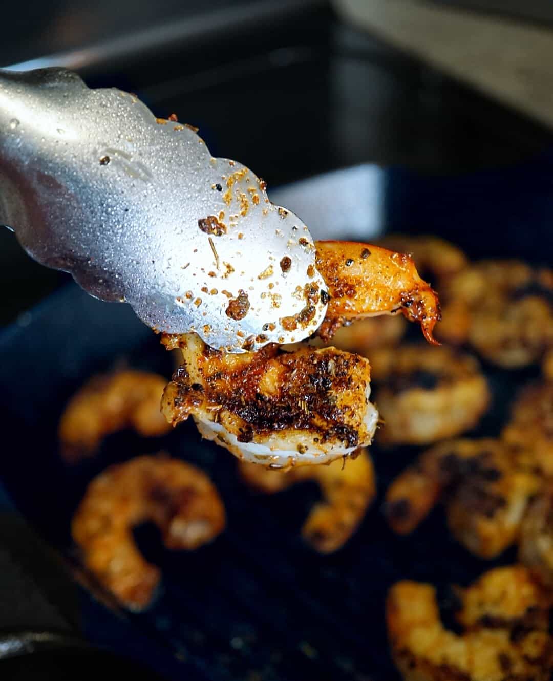 Tongs holding a blackened shrimp