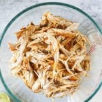 slow cooker pulled chicken in a glass bowl with limes and cilantro