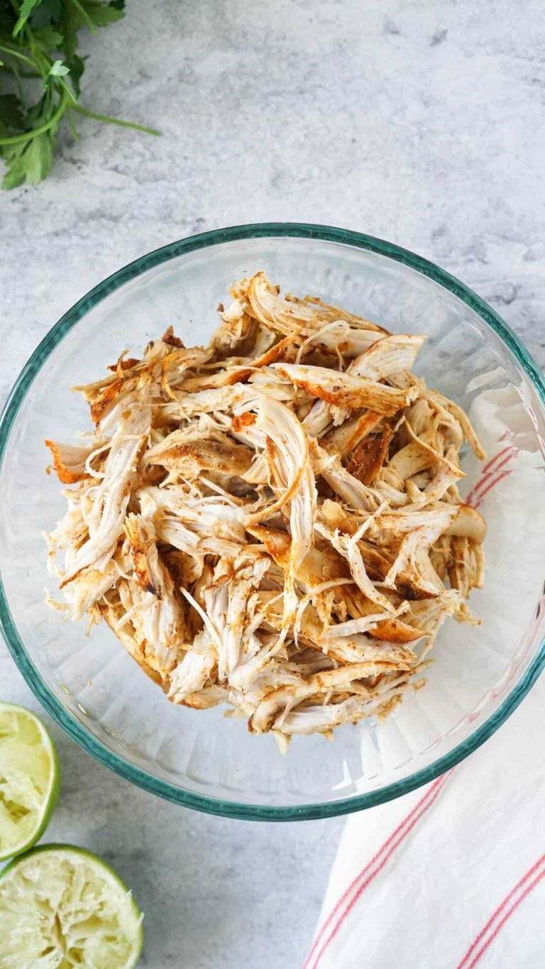 slow cooker pulled chicken in a glass bowl with limes and cilantro