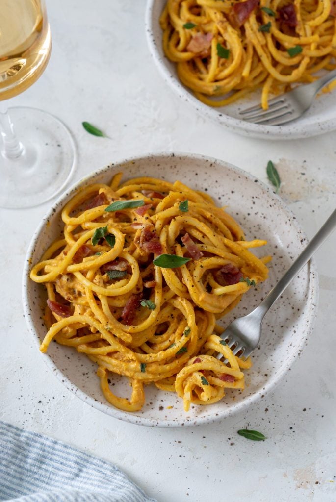 two white bowls of pumpkin pasta with a glass of wine