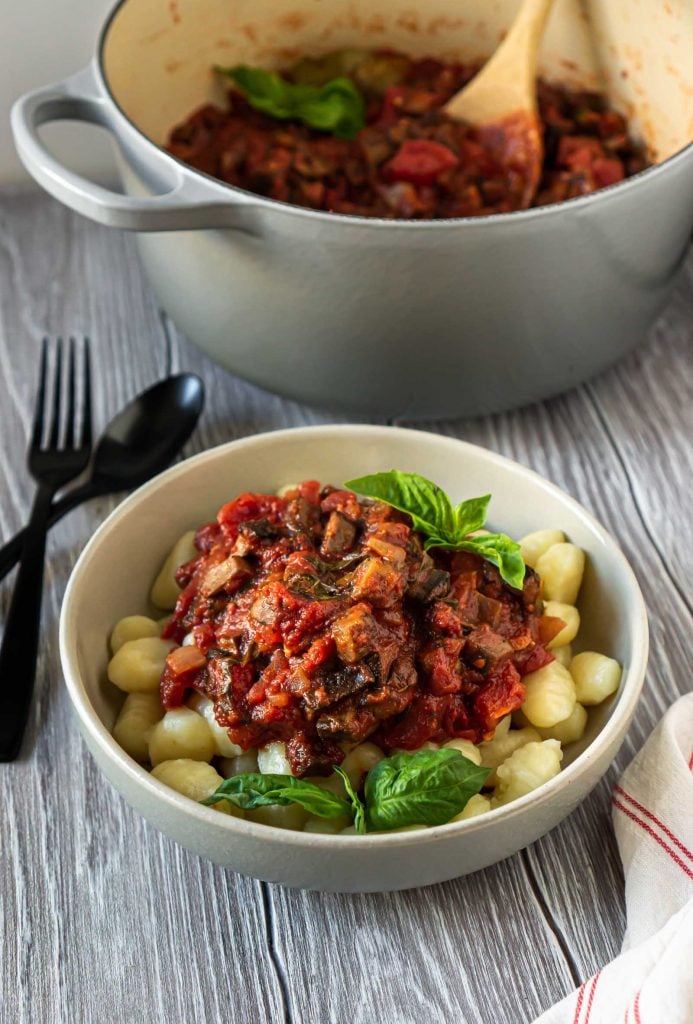 a bowl with gnocchi and mushroom bolognese with a large grey pot