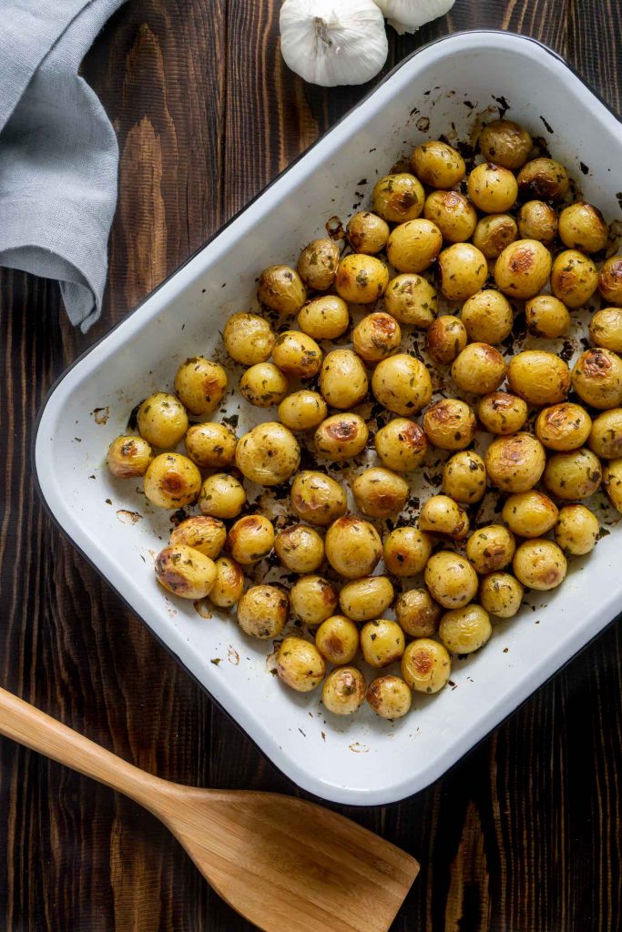 roasted mini potatoes in a white baking pan and garlic on the side