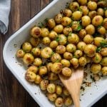 roasted mini potatoes in a white baking dish with a wooden spoon