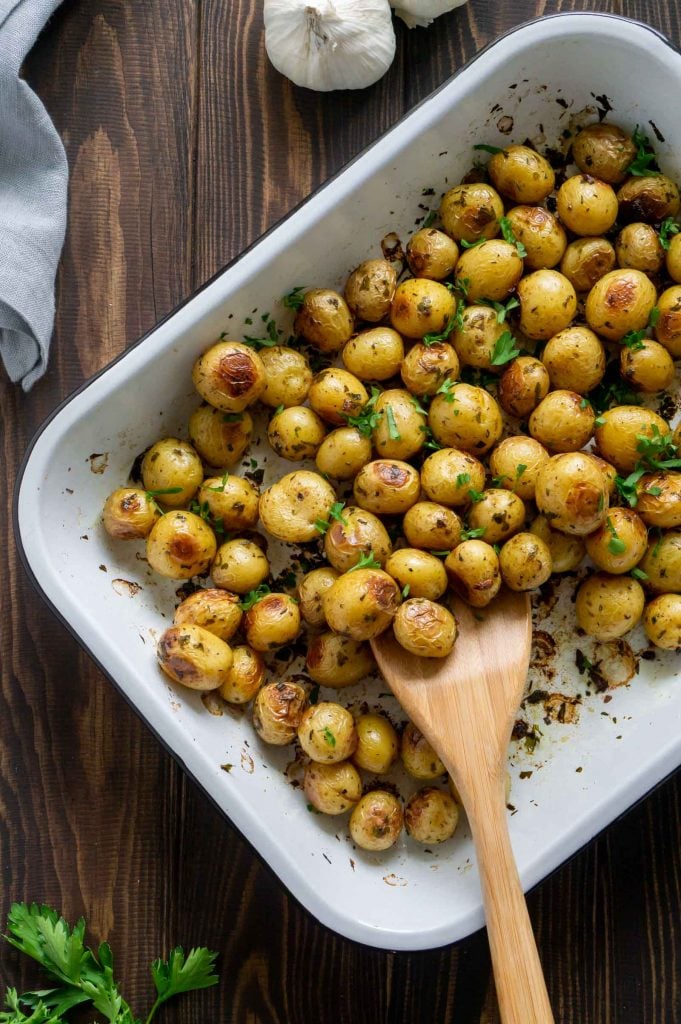 roasted mini potatoes in a white baking dish with a wooden spoon