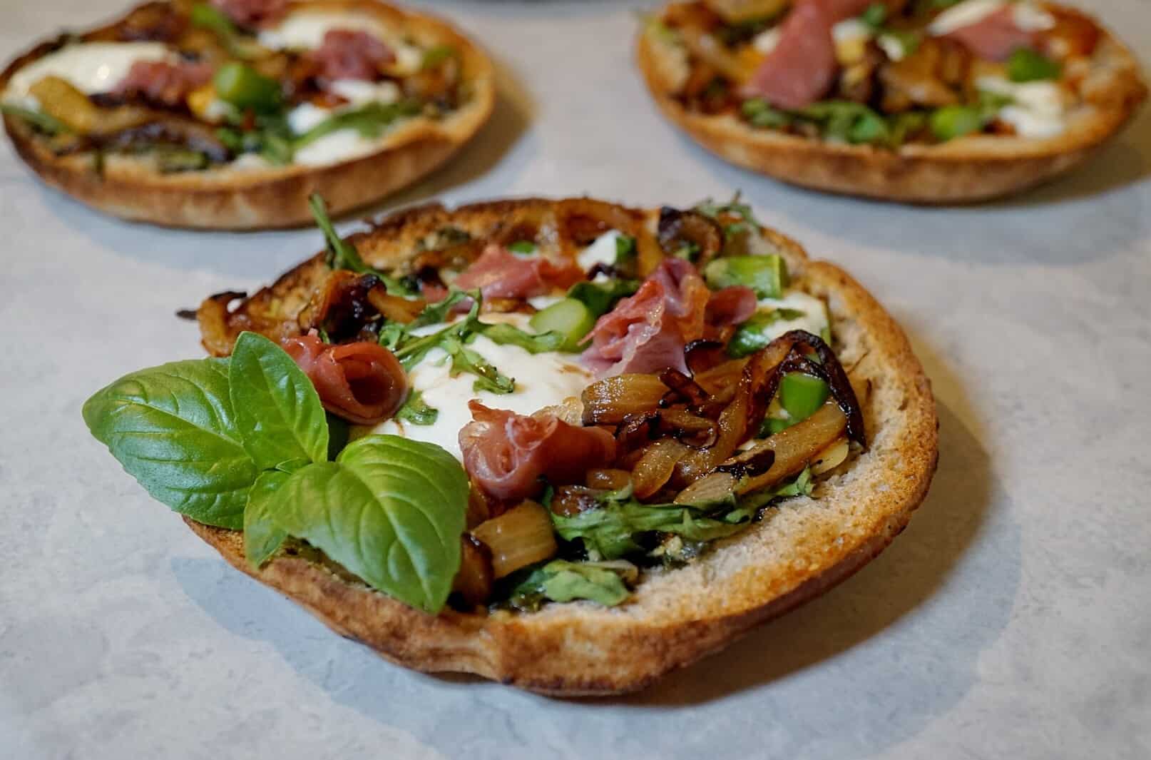 These easy Burrata Pesto Pizzas are the perfect appetizer or even filling enough for a small meal. They're made with Filippo Berio Pesto, prosciutto, burrata cheese, caramelized onions, arugula, and asparagus. These pizzas may be mini, but each bite is like a flavor explosion in your mouth!