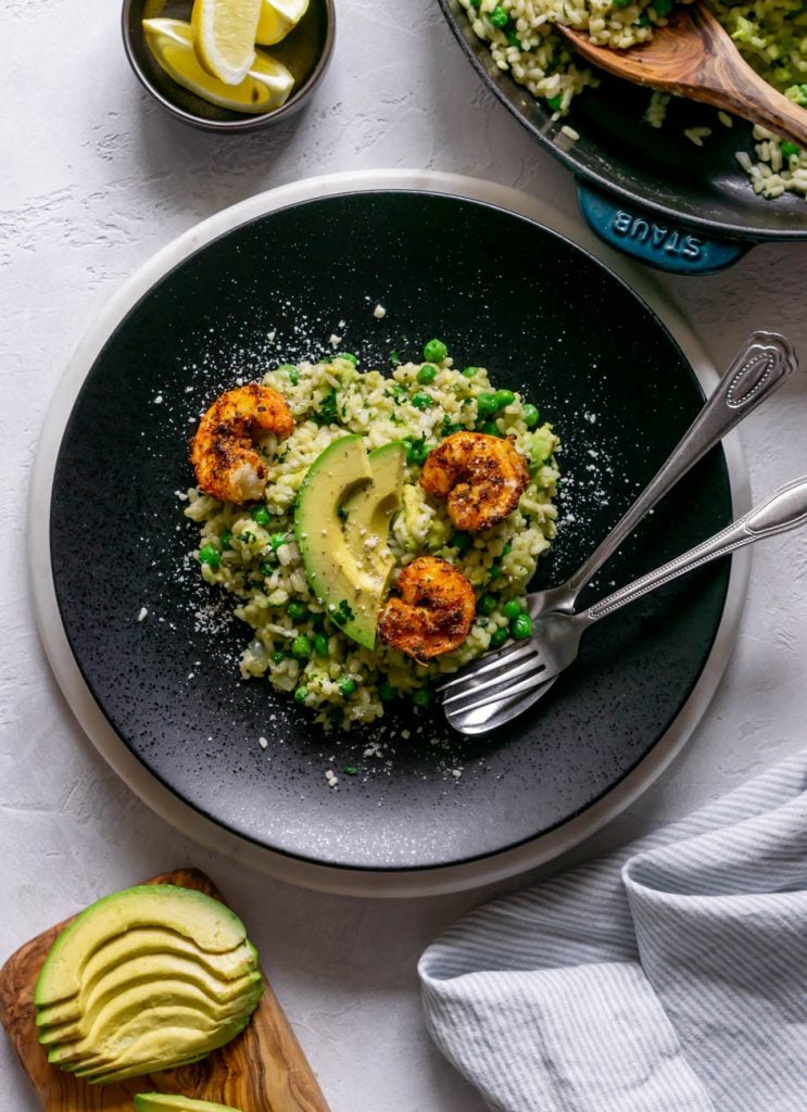 blackened shrimp with avocado risotto on a black plate with a silver fork and spoon