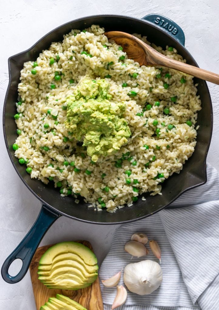 arborio rice in a skillet with a wooden spoon and avocado