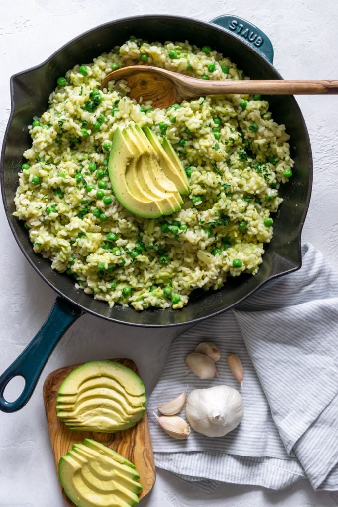 vegan avocado risotto in a skillet with a wooden spoon and sliced avocado