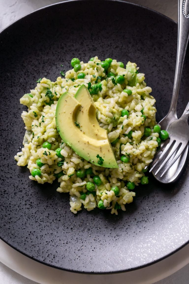 avocado risotto on a black plate with a silver fork and spoon