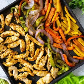 whole30 sheet pan fajitas on a baking sheet with salsa and guacamole