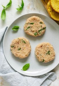 three chicken patties on a white plate with basil leaves