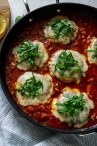 chicken parmesan burgers in a pan with tomato sauce and basil
