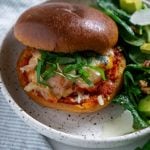chicken parmesan burger on a white plate with salad