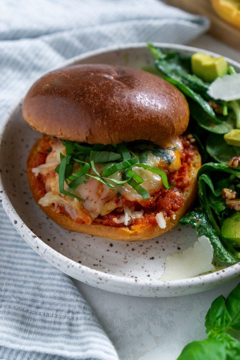 chicken parmesan burger on a white plate with salad