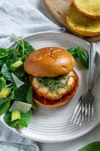avocado salad and chicken burger on a white plate with two forks