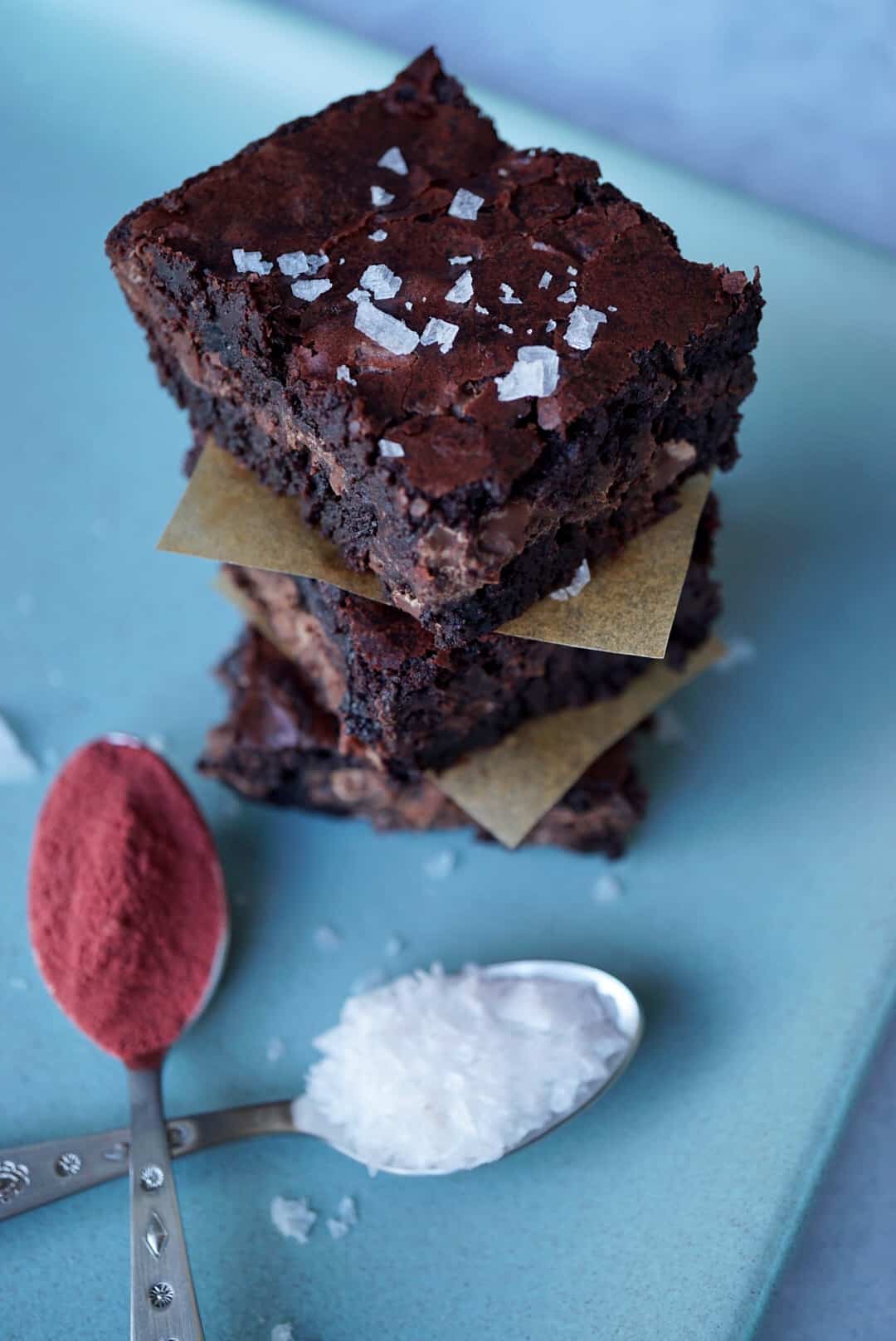 Three brownies stacked with two spoons of beetroot powder and flaky salt