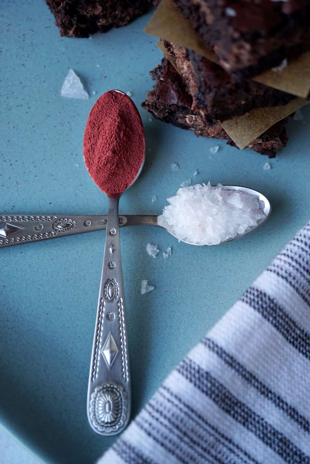 Two spoons of beetroot powder and flaky salt with brownies stacked above