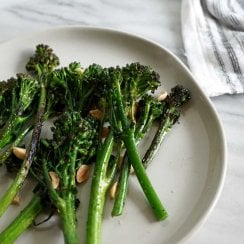 Broccolini and marcona almonds on a white plate with a striped dish towel