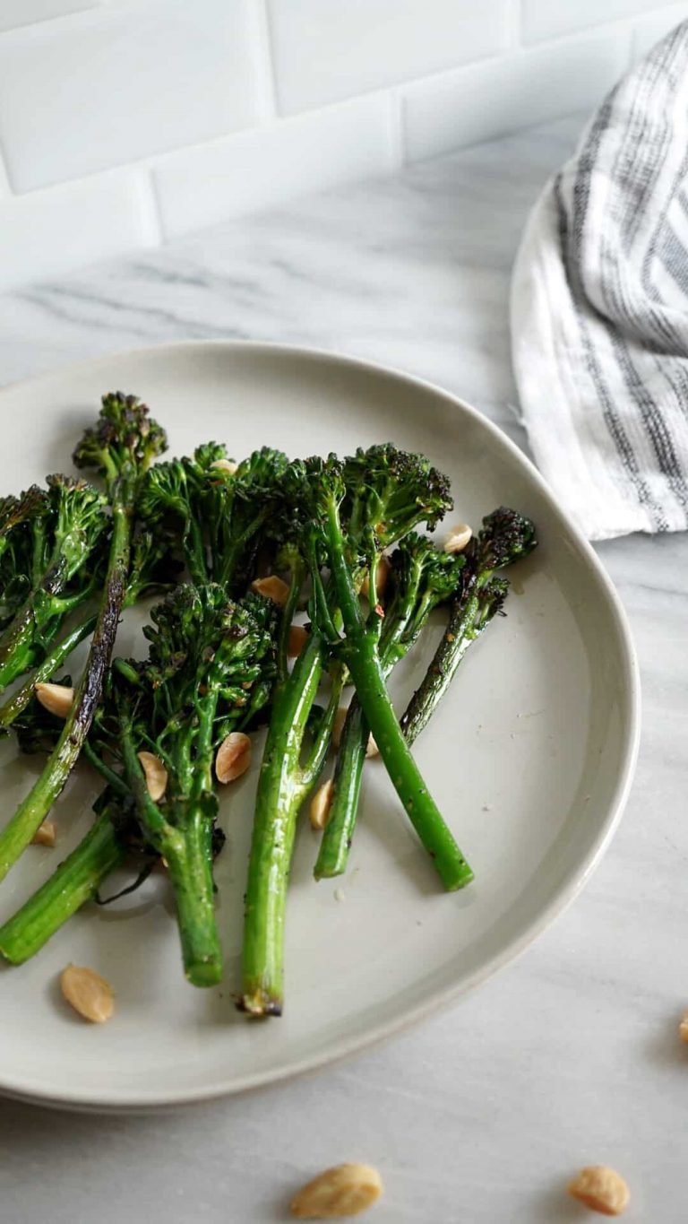 Broccolini and marcona almonds on a white plate with a striped dish towel