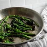 Sauteed broccolini in a silver skillet with a striped towel