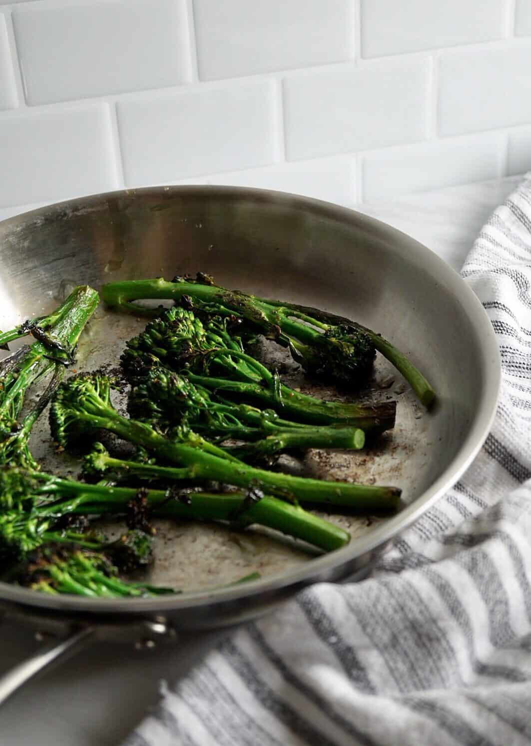 Broccolini in a silver skillet with a striped towel