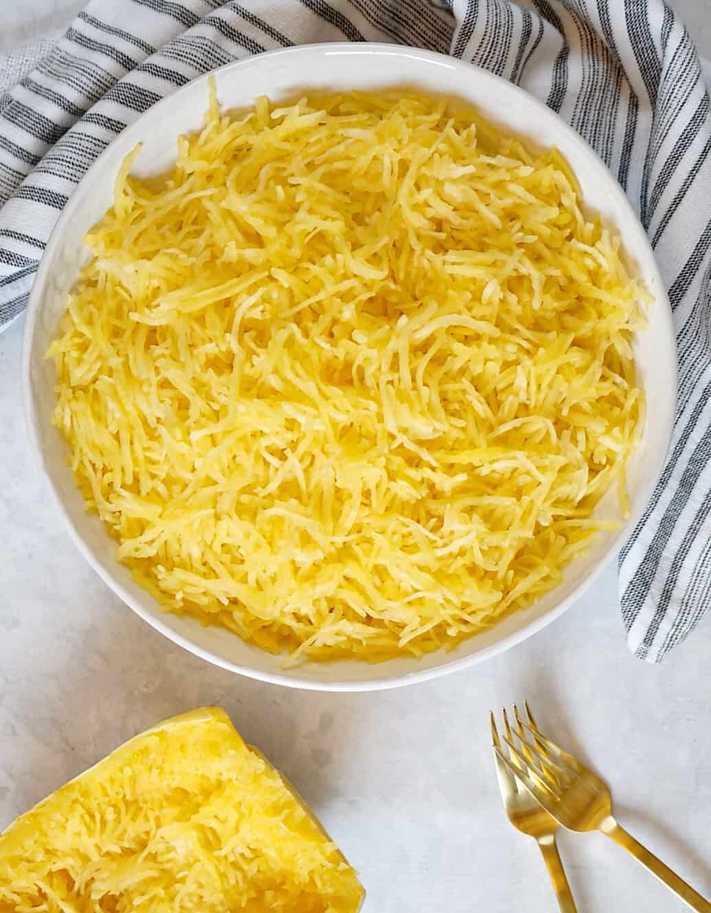 Spaghetti squash in a white bowl with two gold forks