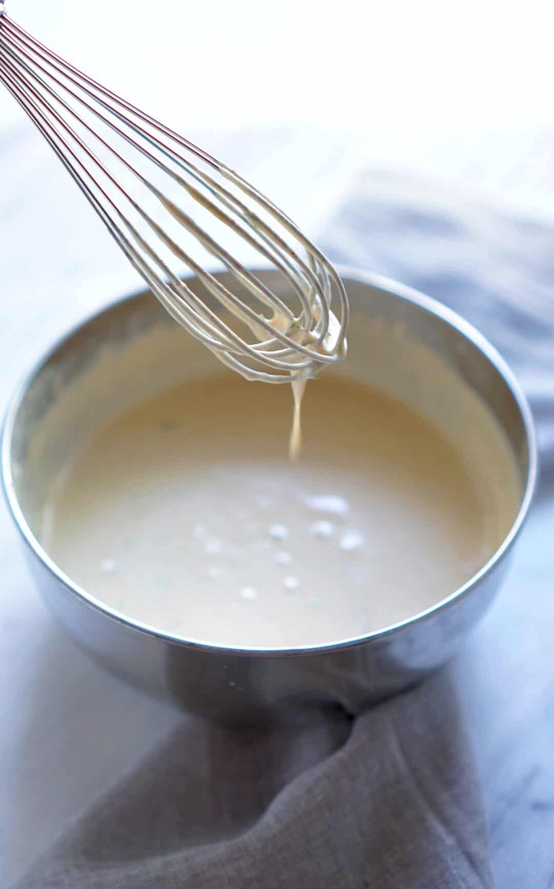 Whisk with tahini sauce dripping into a metal bowl