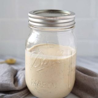 Tahini sauce in a mason jar with a white tile background