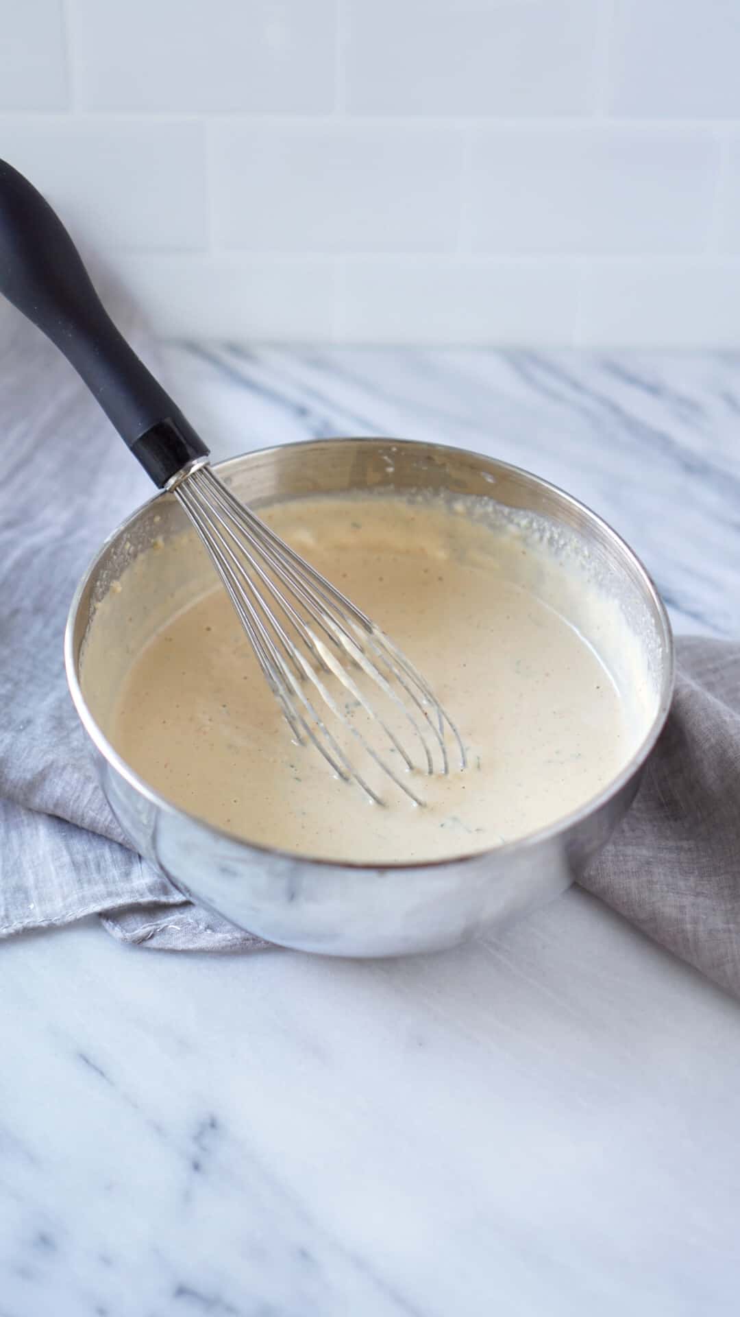 Whisk in a metal mixing bowl with tahini sauce