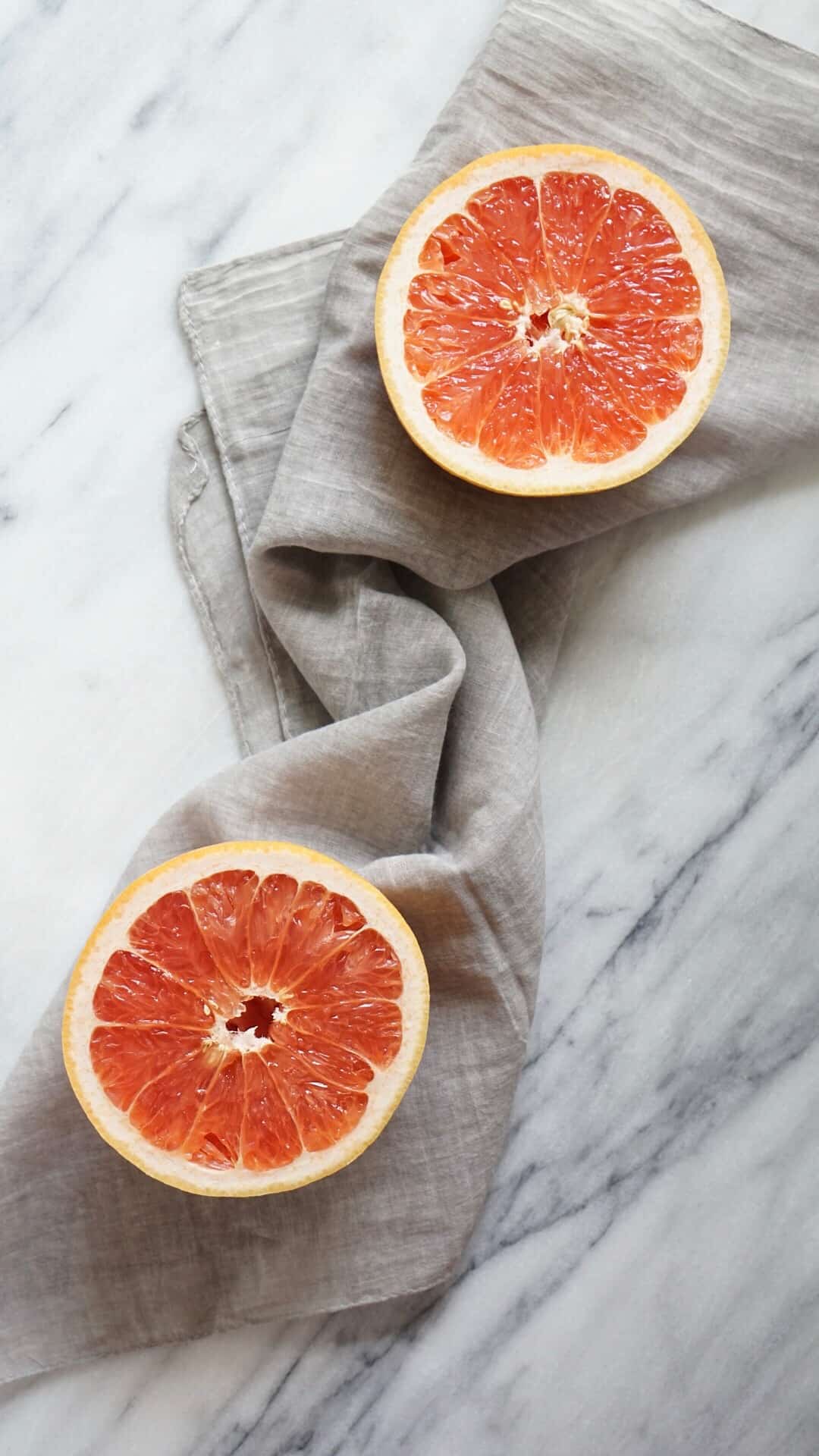Two grapefruit halves on a grey napkin with a marble background