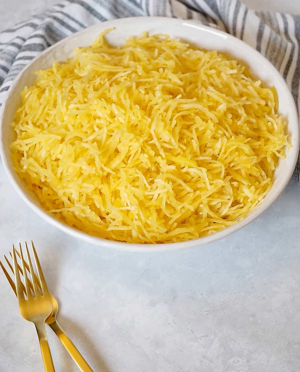 Spaghetti squash in a white bowl with two gold forks