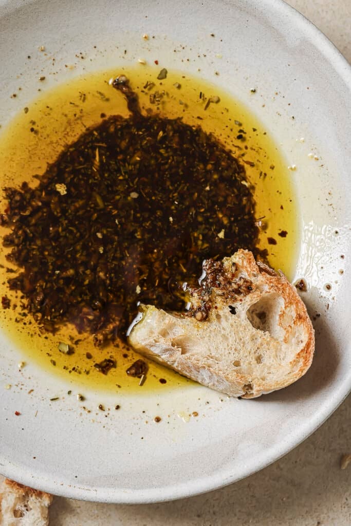 close up photo of a piece of bread in a white bowl with olive oil bread dip