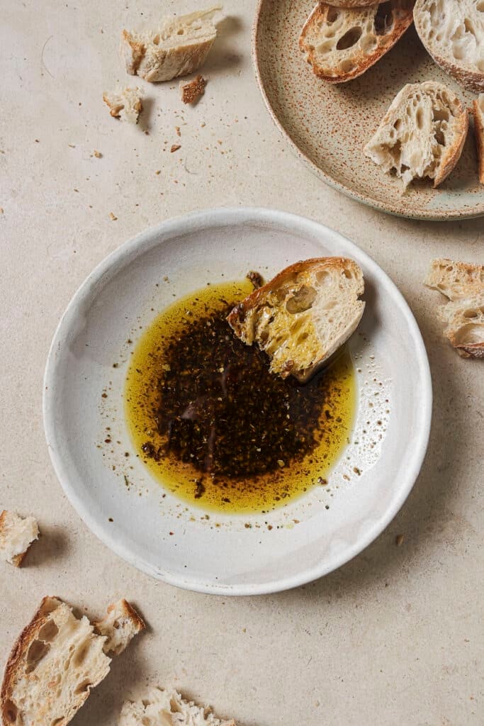 a piece of sourdough bread in a white bowl with olive oil bread dip