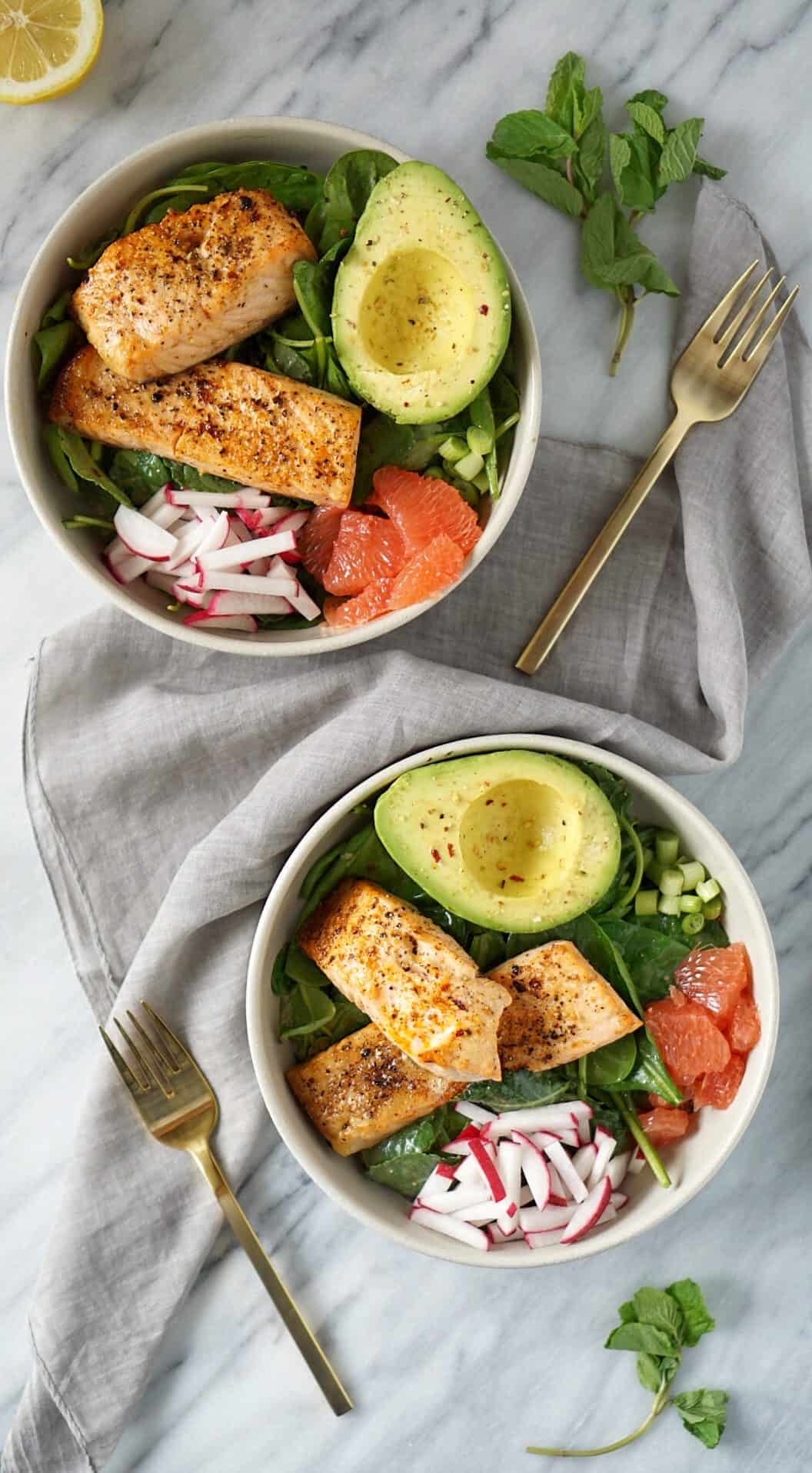 two salmon bowls with a grey napkin and gold fork