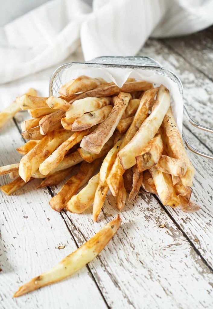 Air fryer french fries spilling out of a basket with ketchup