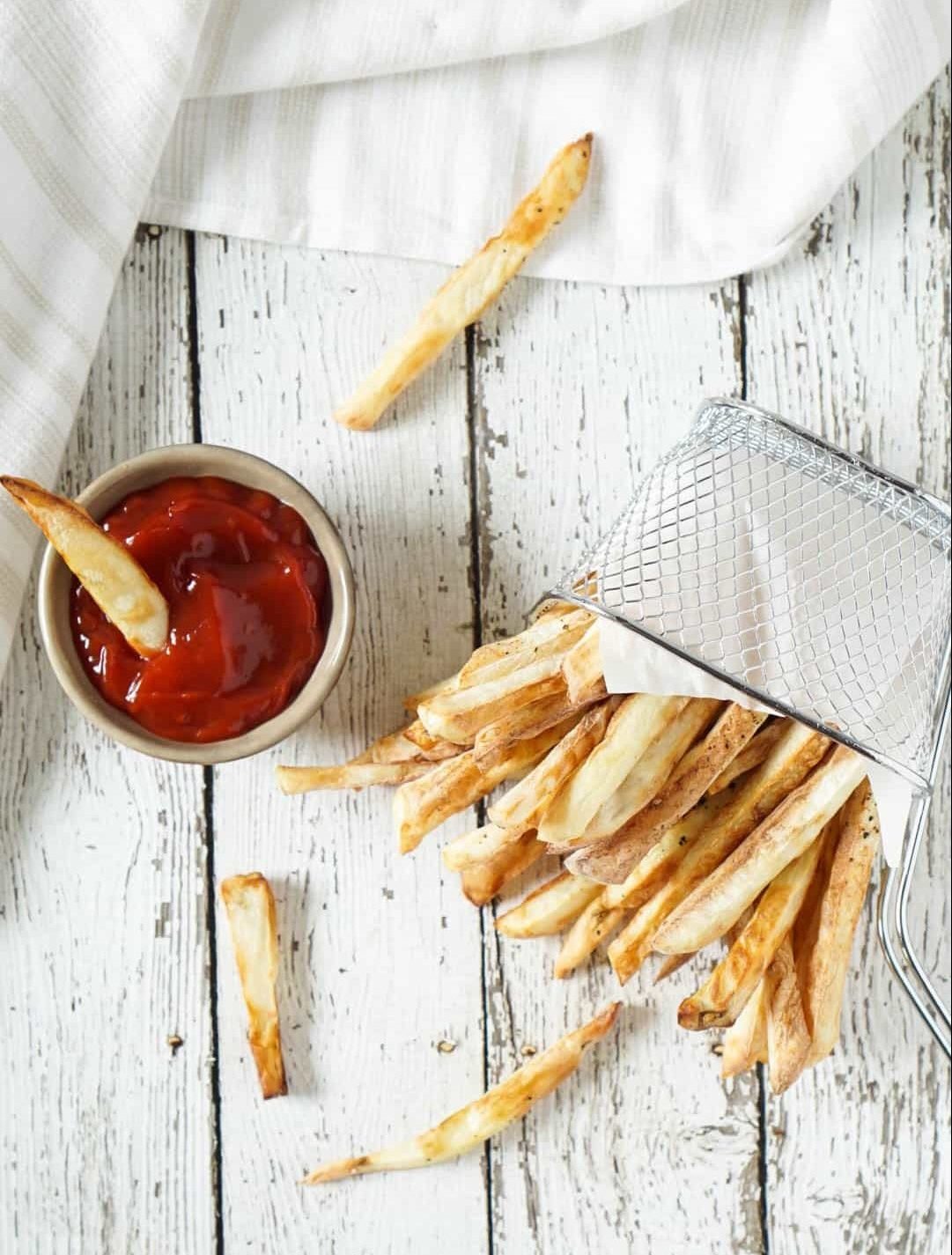 air fryer french fries spilling out of a basket with ketchup