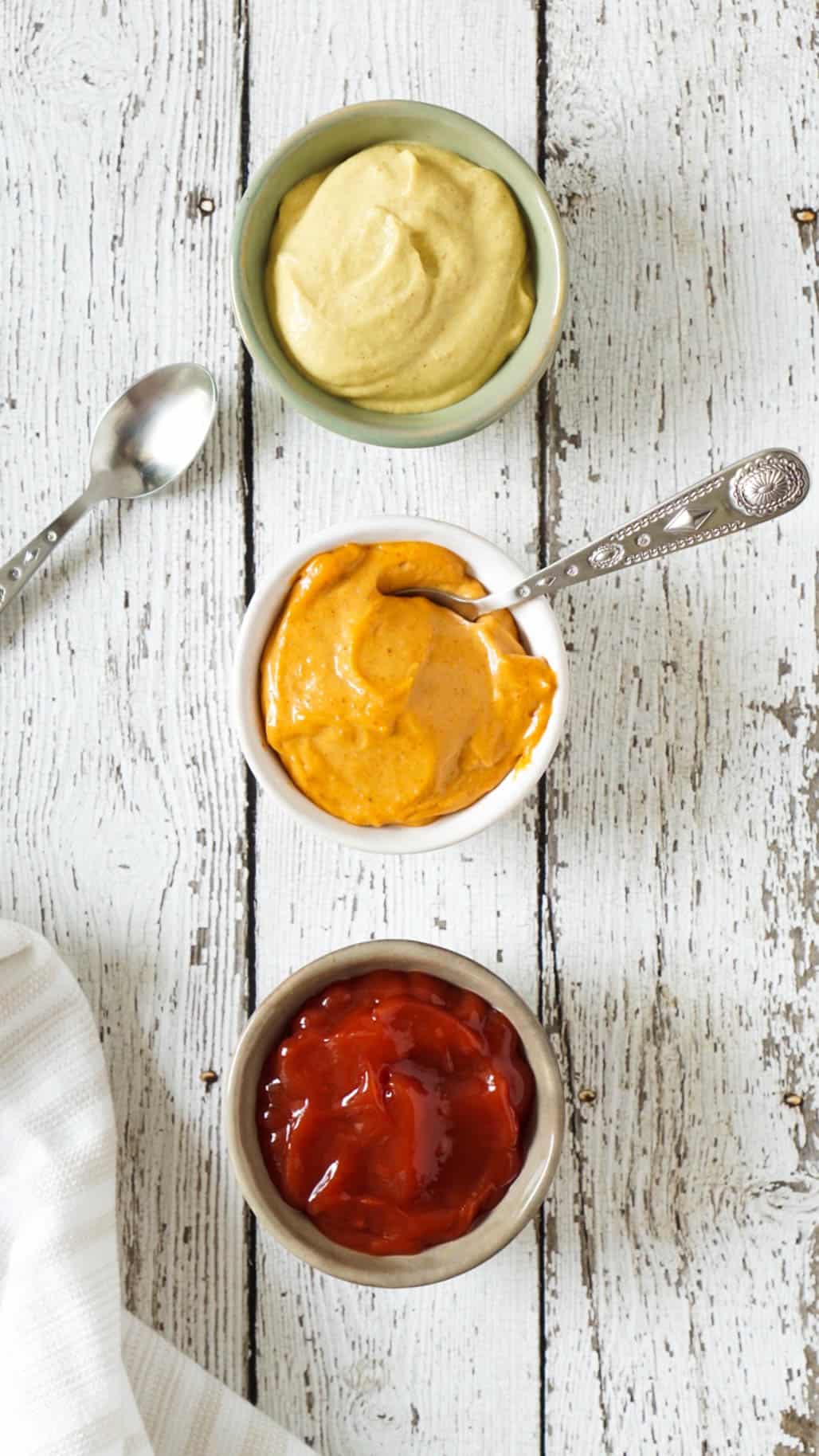 ketchup and mustard in 3 small bowls with silver spoons
