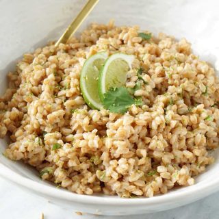 Cilantro lime farro in a white bowl with gold utensils