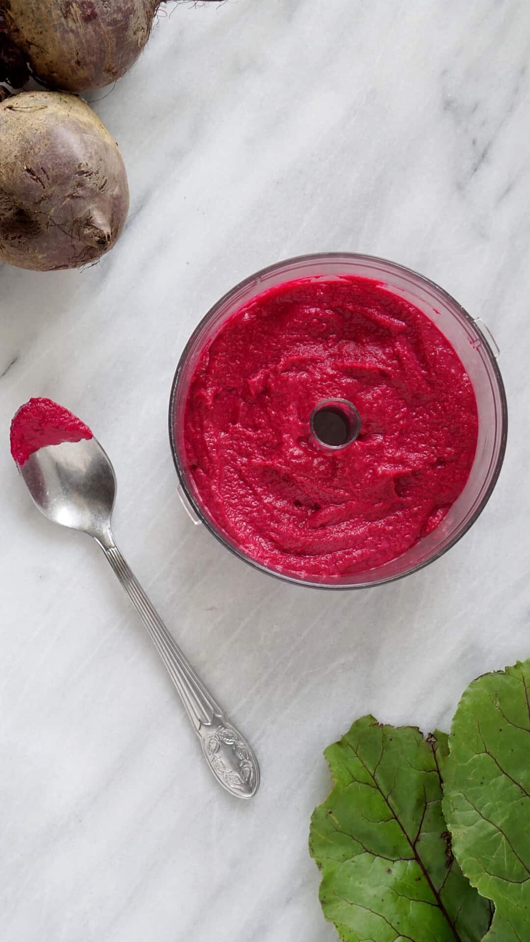 Beet hummus in a food processor with a silver spoon