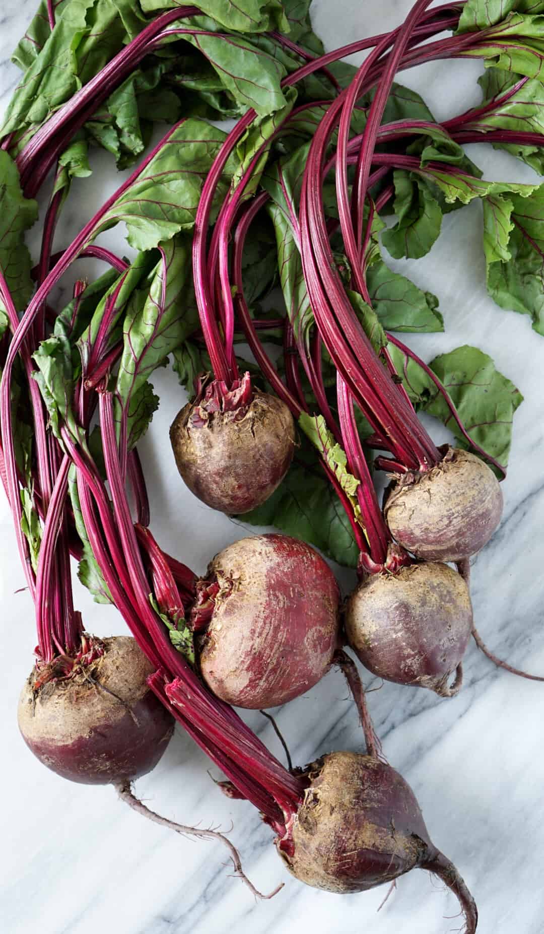 Six beets bunched together on a marble slab