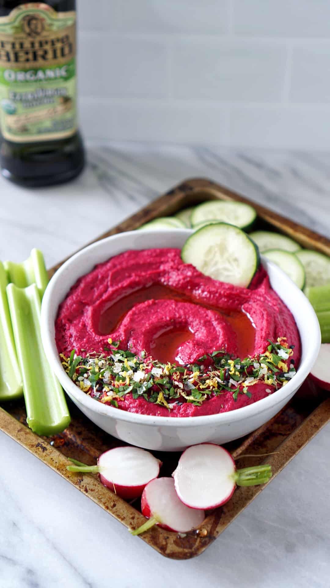 Cucumber dipped in beet hummus with vegetables on a tray