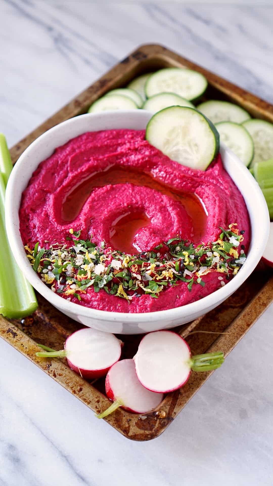 Roasted beet hummus in a bowl with vegetables on a tray