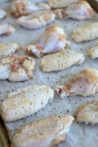 Chicken wing sections seasoned with salt, pepper and garlic powder on parchment paper.