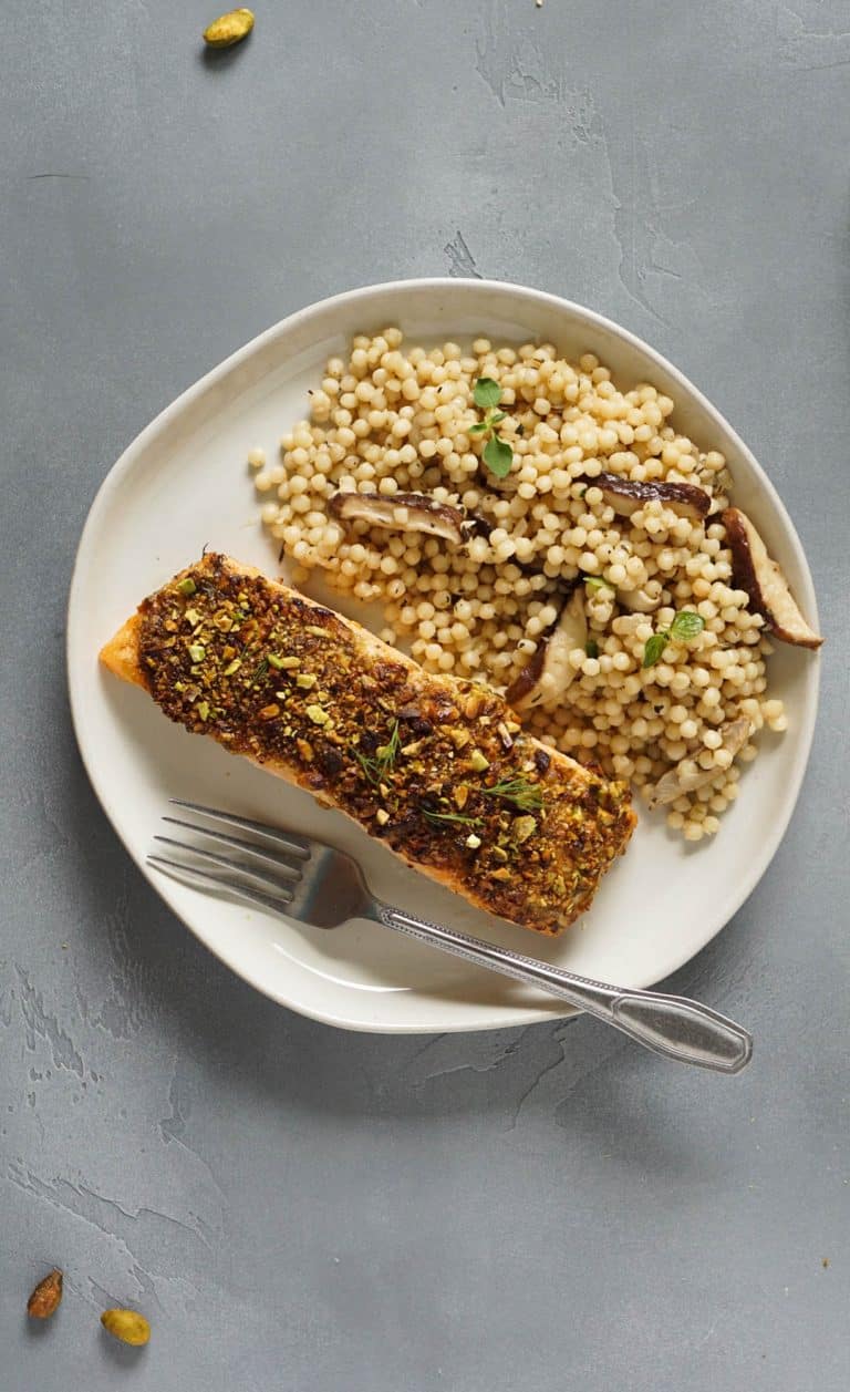 salmon on a white plate with israeli couscous and a fork