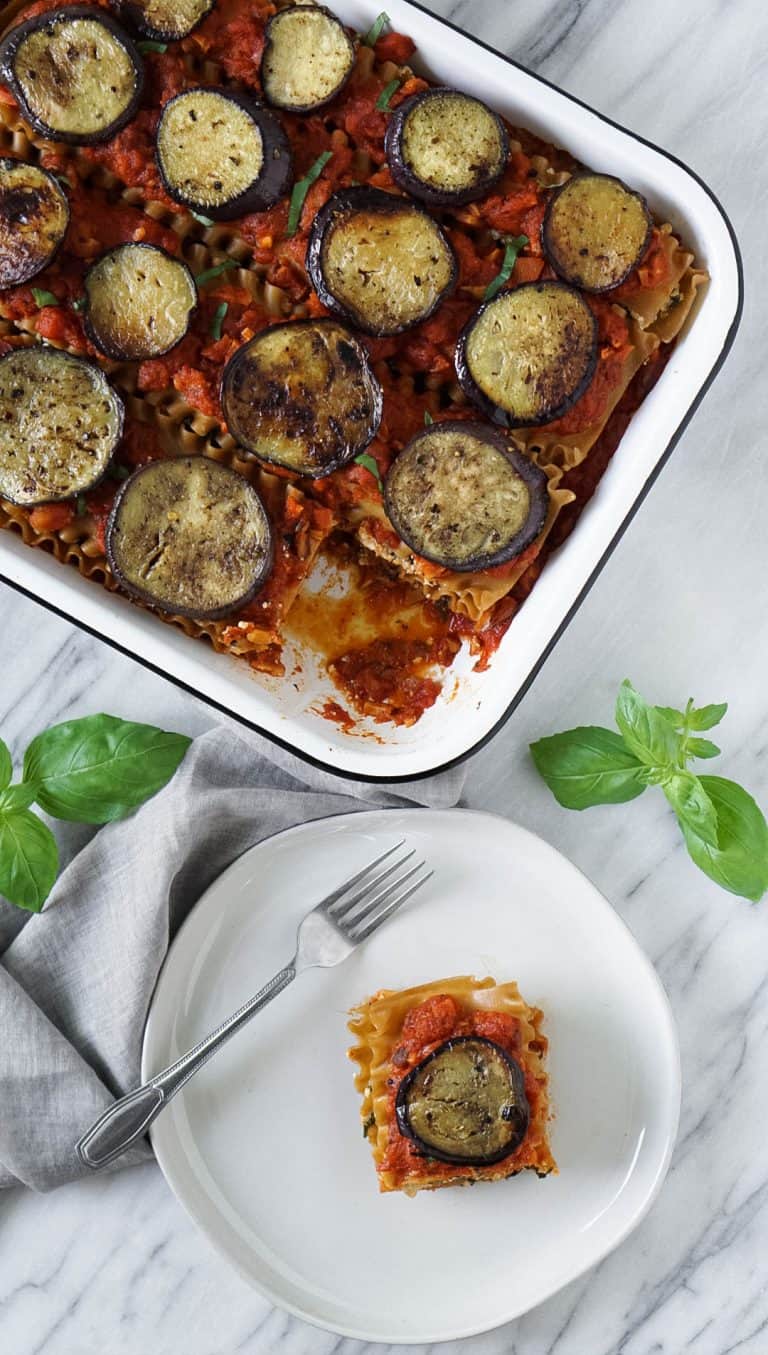 A piece of vegan lasagna on a plate with a fork and some basil