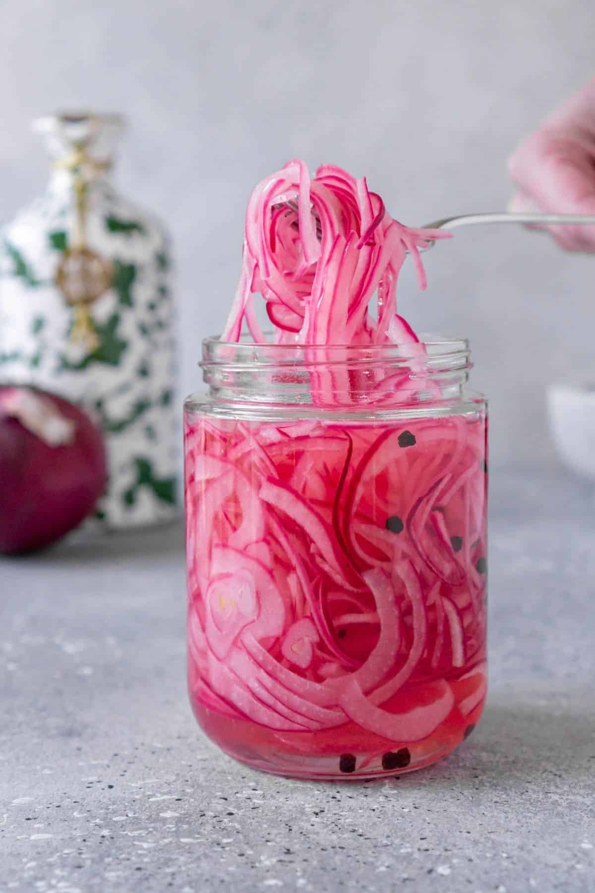 A fork pulls pickled red onions out of a glass jar.