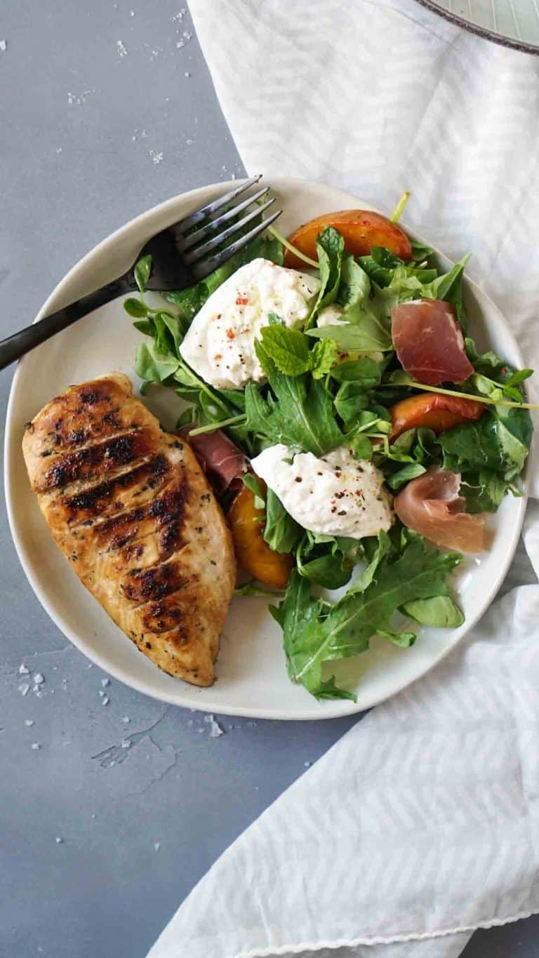 grilled chicken with burrata salad on a plate with a black fork