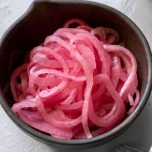 Pickled red onions in a black spouted bowl.